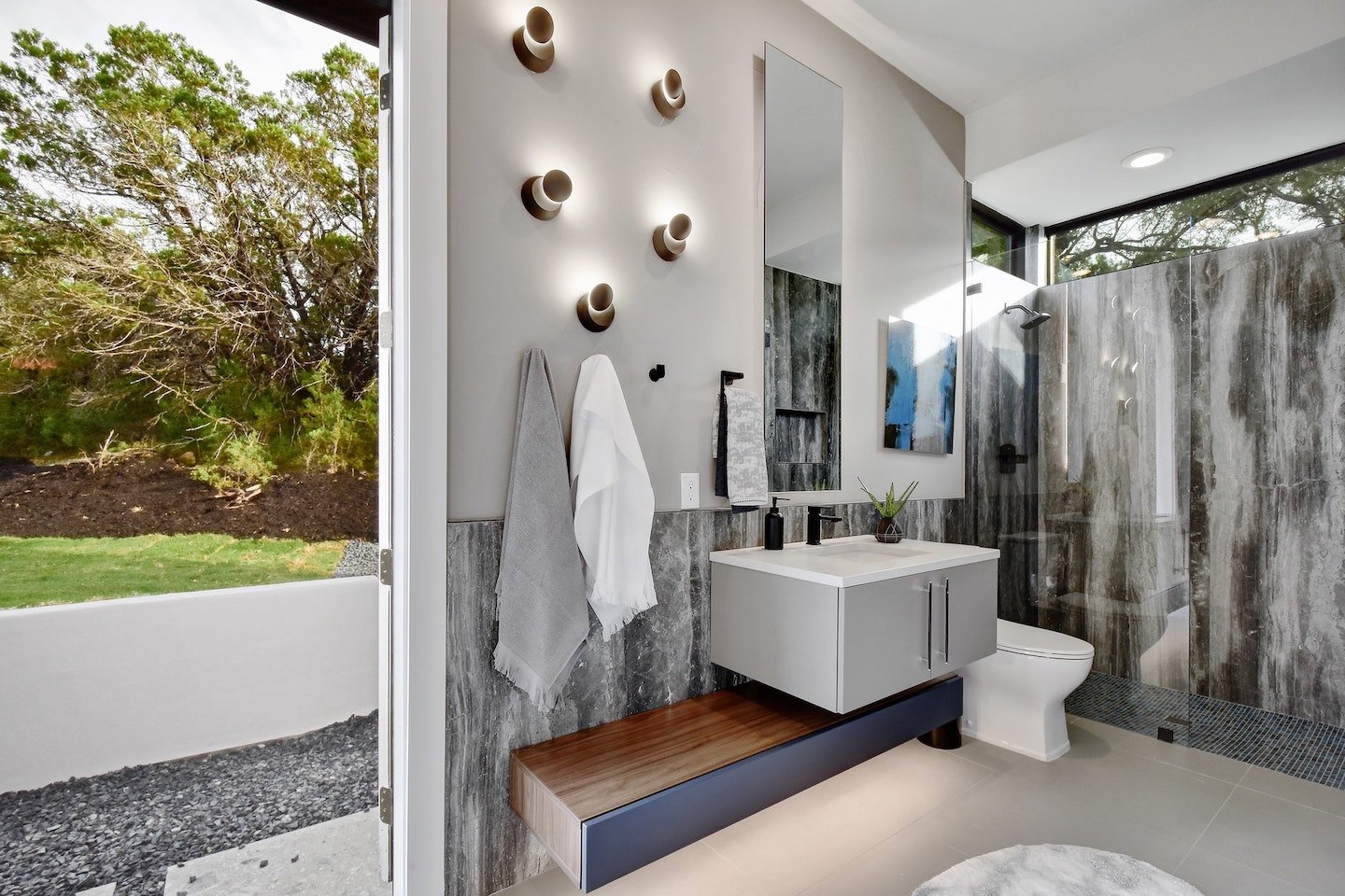 A compact custom bathroom vanity positioned next to a walk-in shower and a doorway looking out to a home’s backyard. 