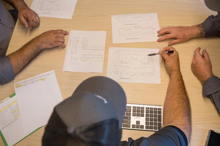 A team of three individuals reviewing design blueprints on a light wood table.