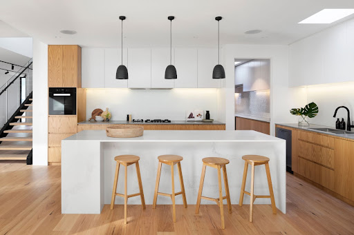 A minimalist kitchen design with white cabinets and light-colored wood.