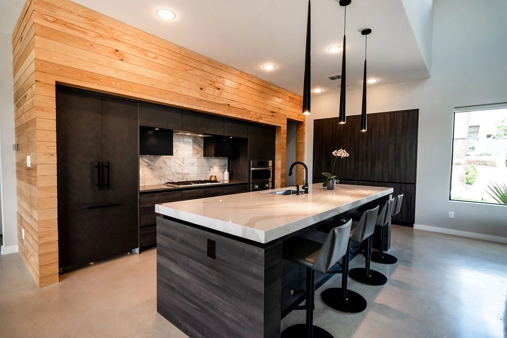 A modern, open kitchen featuring a contrasting light and dark palette. Also in frame is a large kitchen island that includes four barstool seats.