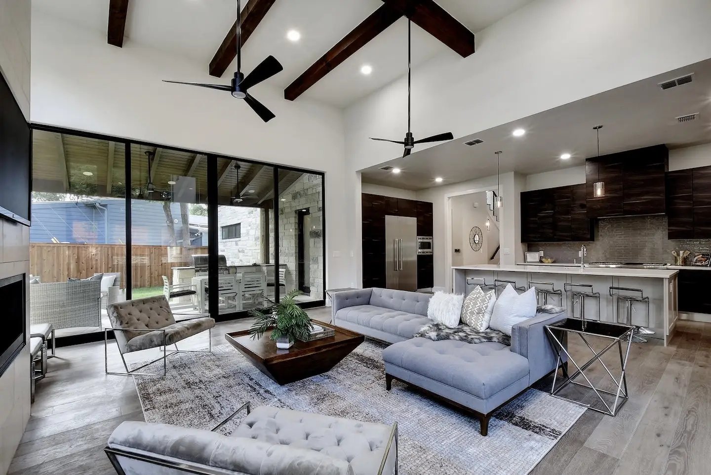 An open, spacious family room that connects to a modern kitchen. In the backdrop, large sliding glass doors look out to the home’s backyard.